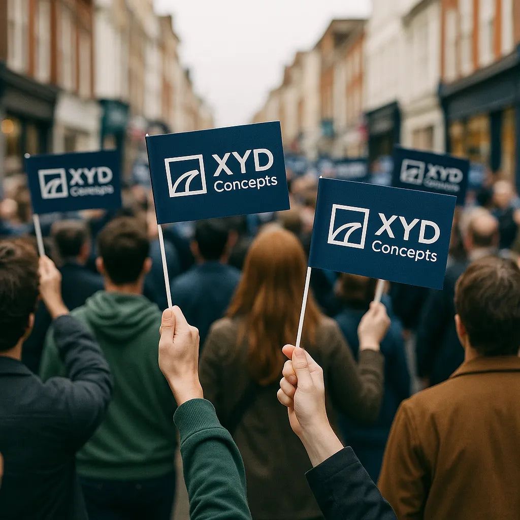 Custom 130 × 205 mm paper hand flags with dark-blue ‘XYD Concepts’ logo on 325 mm paper sticks, waved by a crowd on a high street.