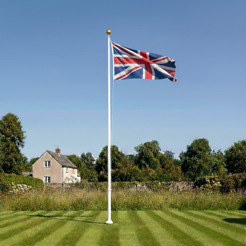 Union Jack flag on a flagpole in a grassy area with a house and trees in the background.