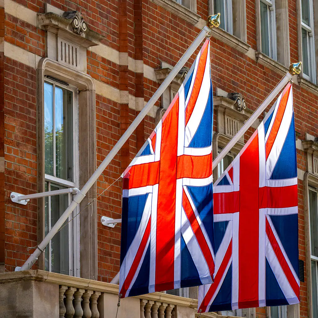 Two angled British flags waving in front of a brick building