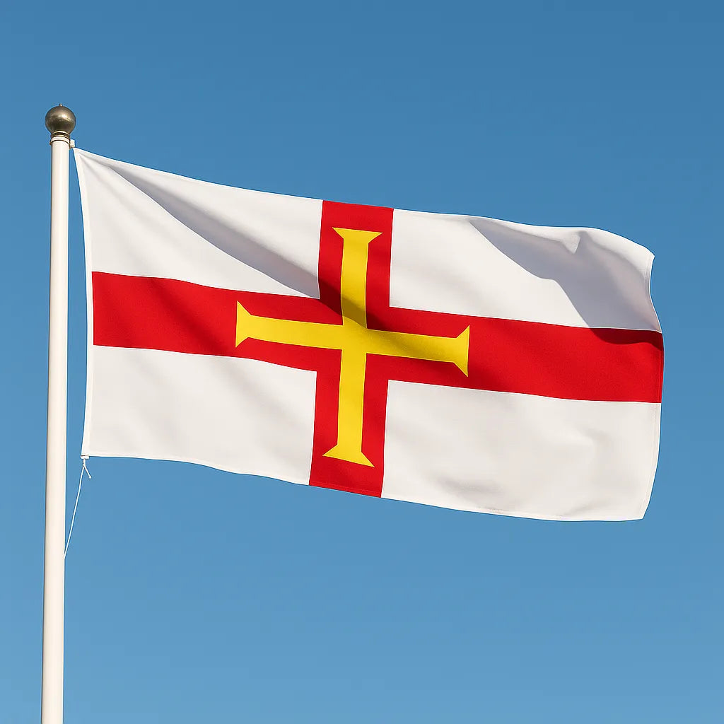 The flag of Guernsey flying on a white flagpole with a gold finial, showing a red cross with a smaller yellow cross inside, set against a clear blue sky.