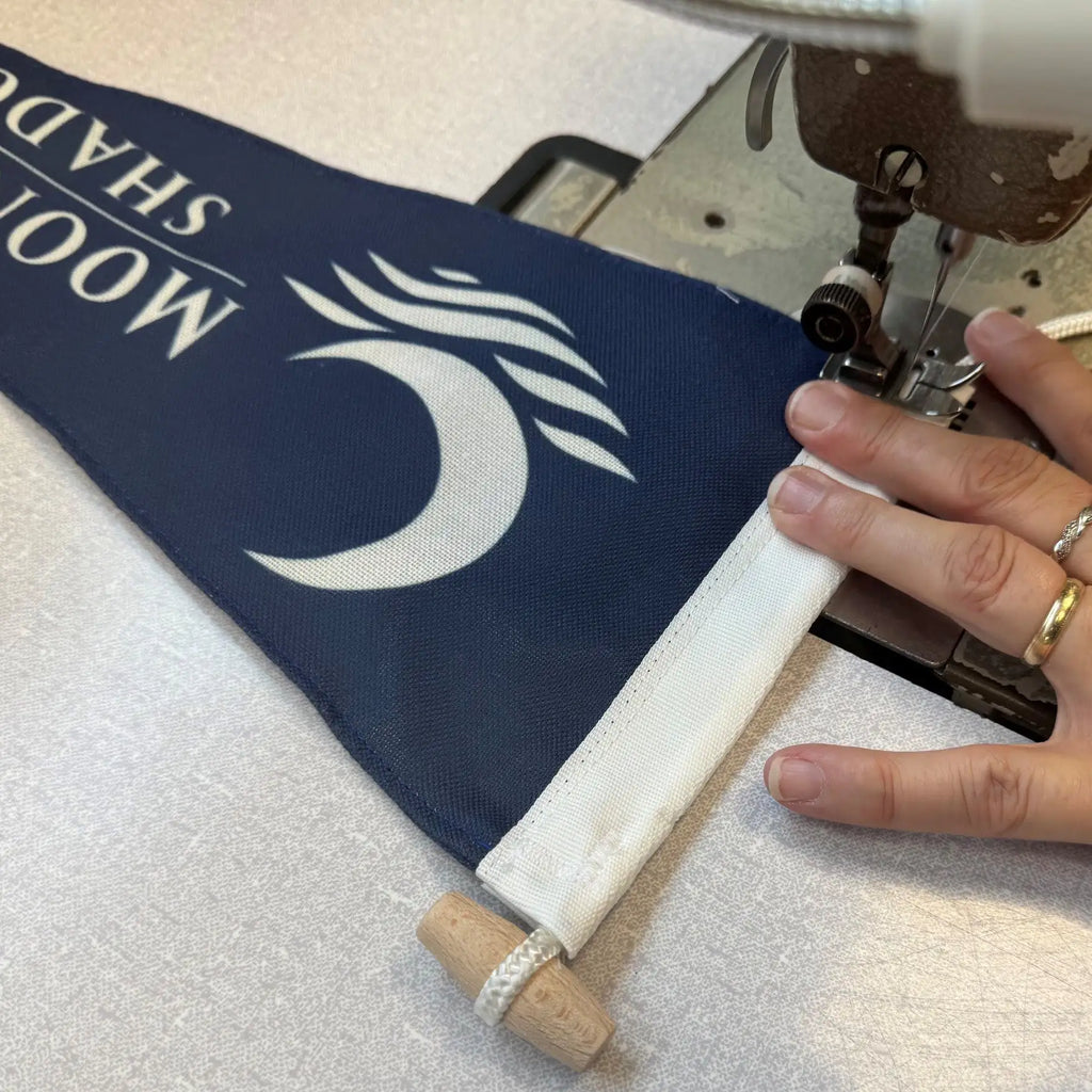 Person using a sewing machine on a blue fabric burgee with white text and design.
