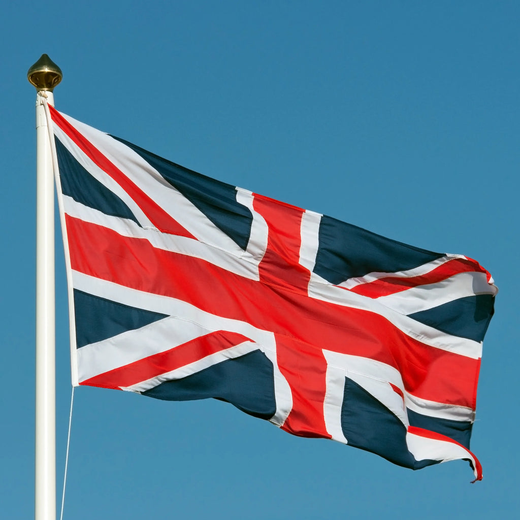 Sewn high-quality Union Jack flag made in the UK, woven polyester fabric with reinforced stitching, flying on a flagpole outdoors.