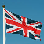 Sewn high-quality Union Jack flag made in the UK, woven polyester fabric with reinforced stitching, flying on a flagpole outdoors.