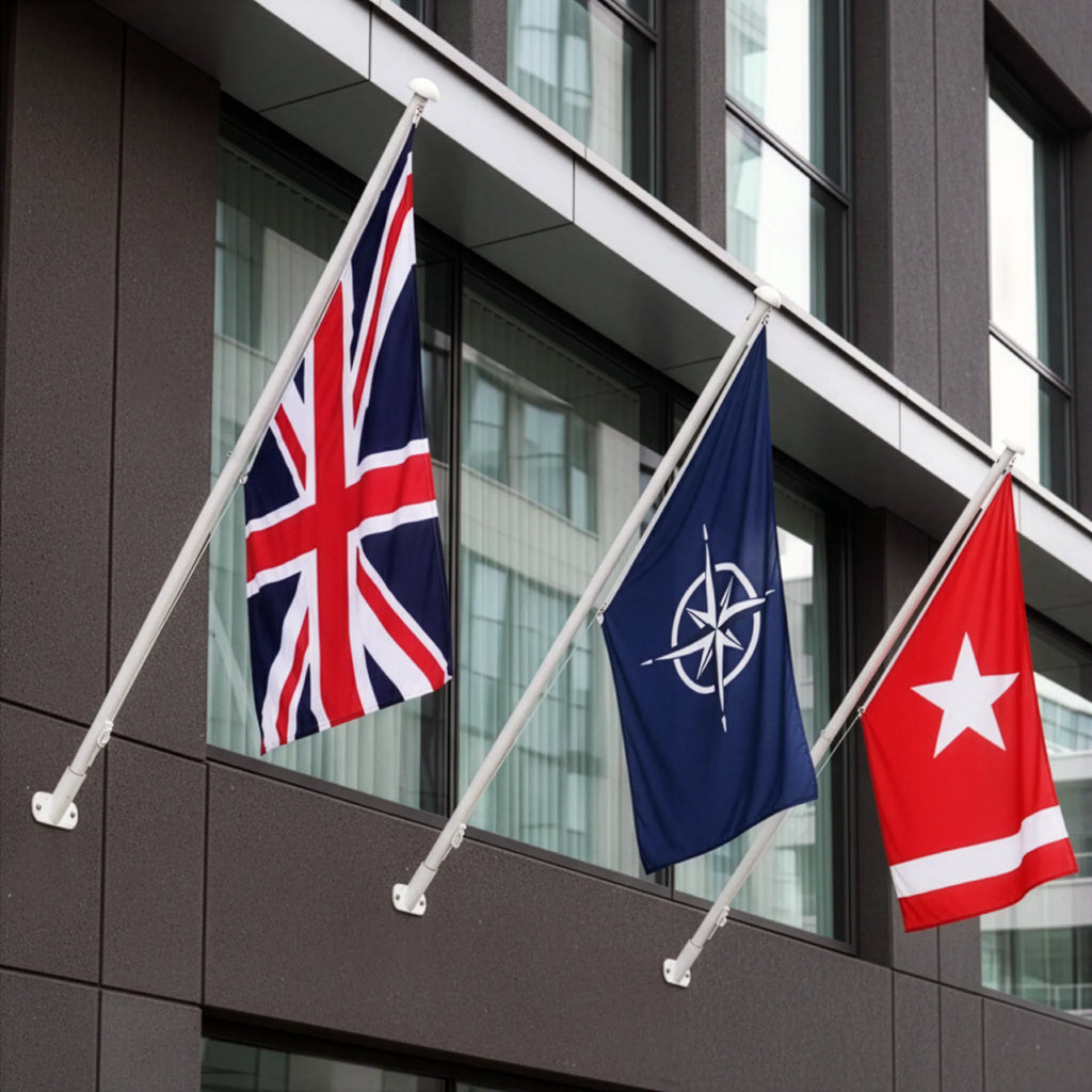 Union Jack flag mounted on a white aluminium wall-mounted flagpole fixed to the façade of a modern brick office building with large glass windows.