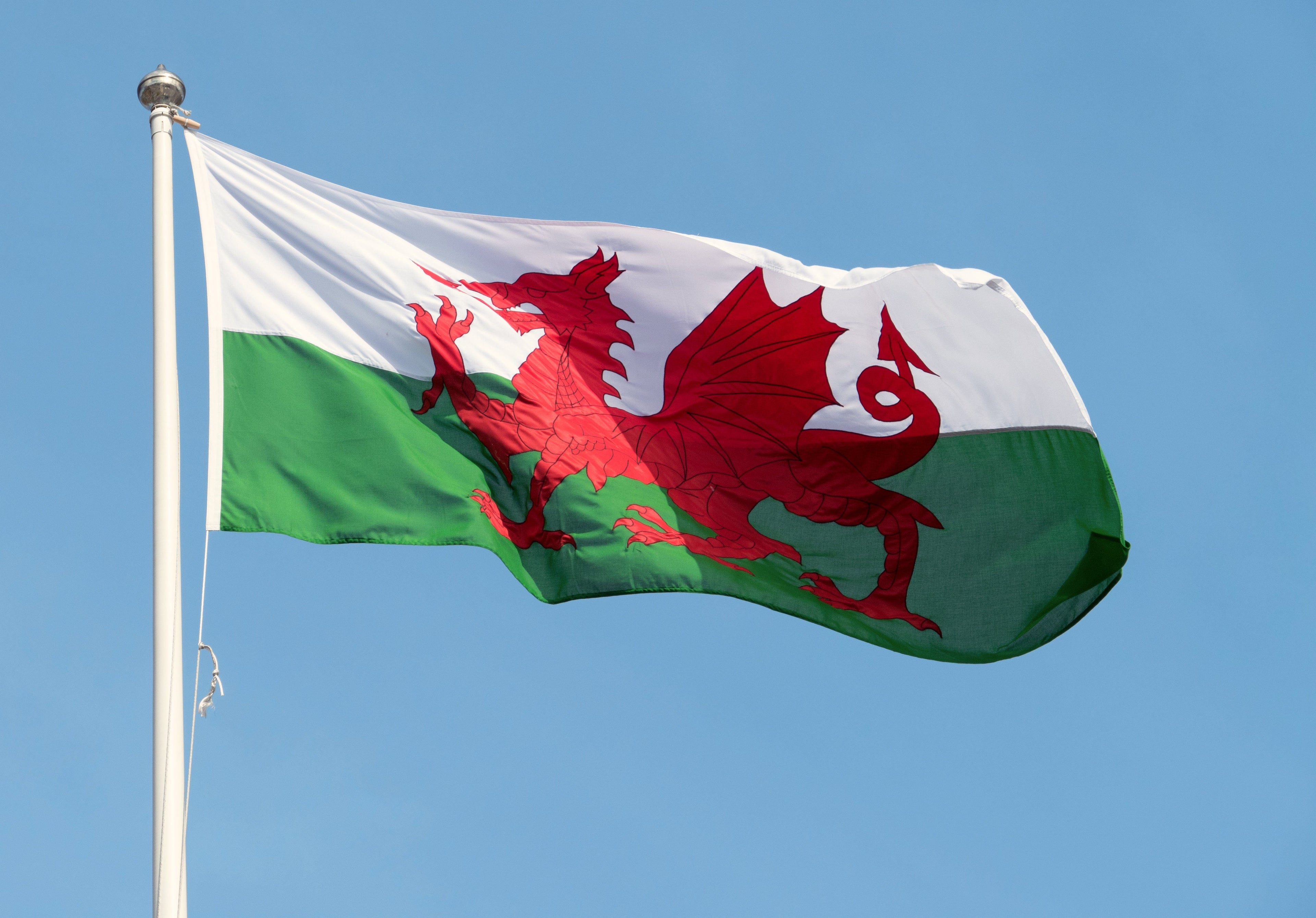 Welsh flag with a red dragon on a white and green background against a clear blue sky.